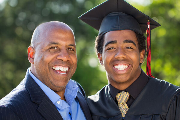 A father with his son, who is dressed in a grad cap and gown image number null